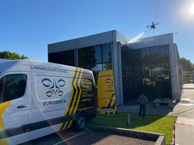 Dron de EURODRON limpiando la fachada de vidrio de un edificio de oficinas en Pozuelo de Alarcón, con la furgoneta de la empresa en primer plano
